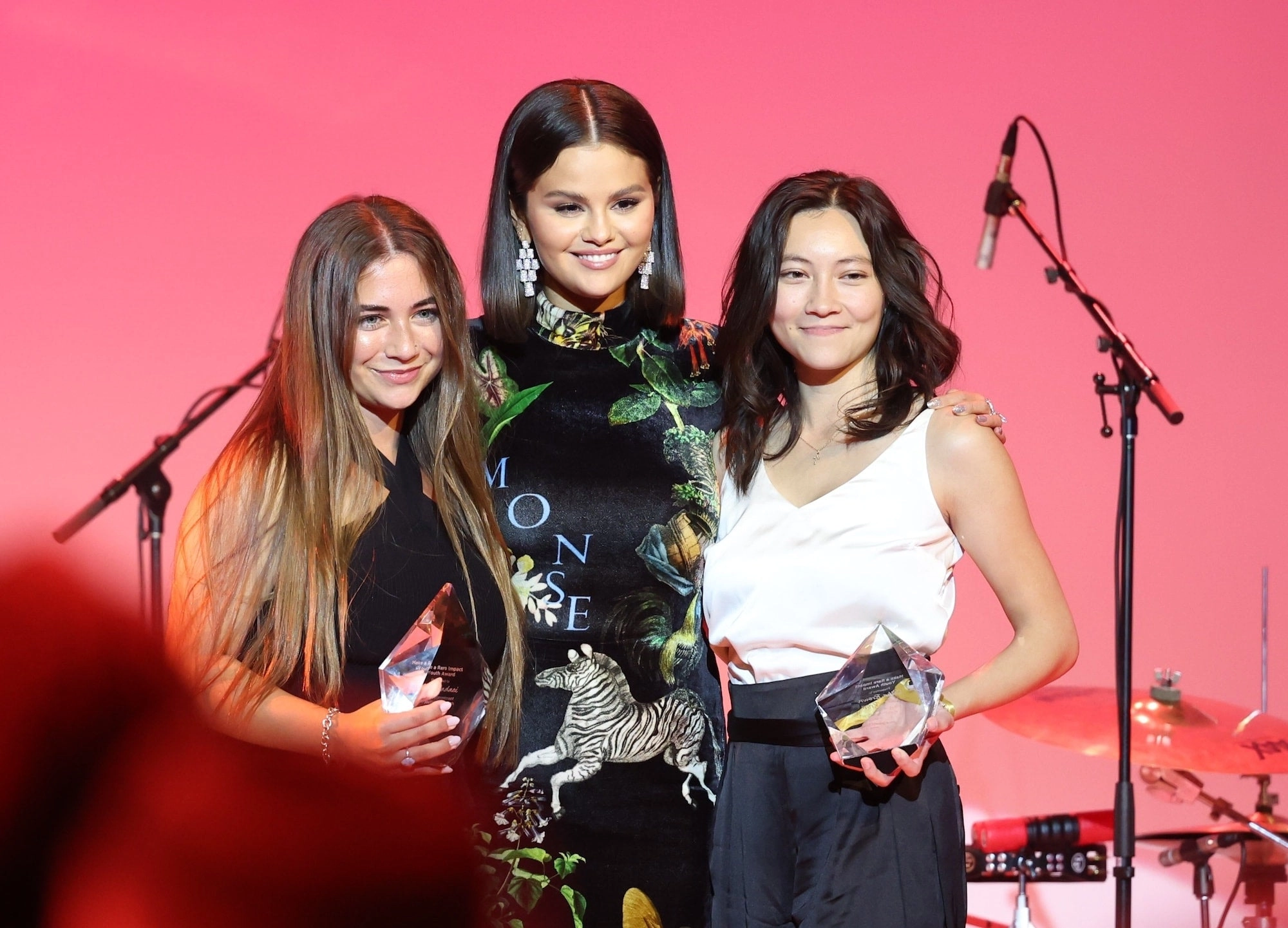 Selena Gomez on stage with two young women under pink light